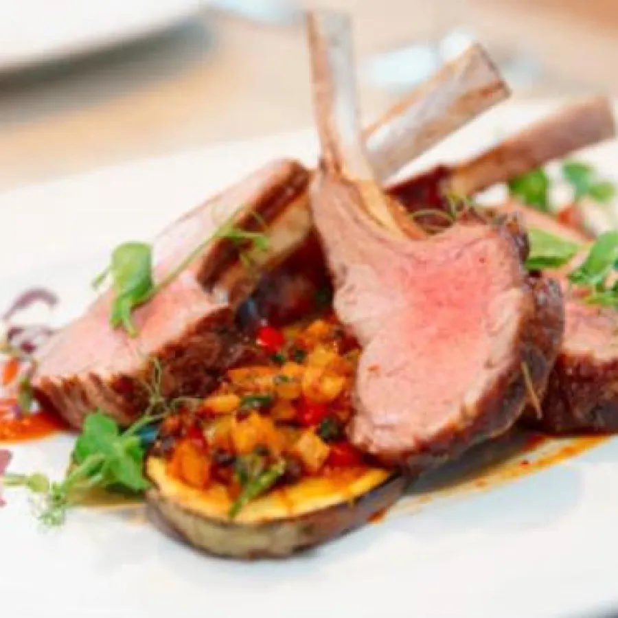 côtes d'agneau cuisinées dans une assiette avec des légumes, de la sauce et des herbes