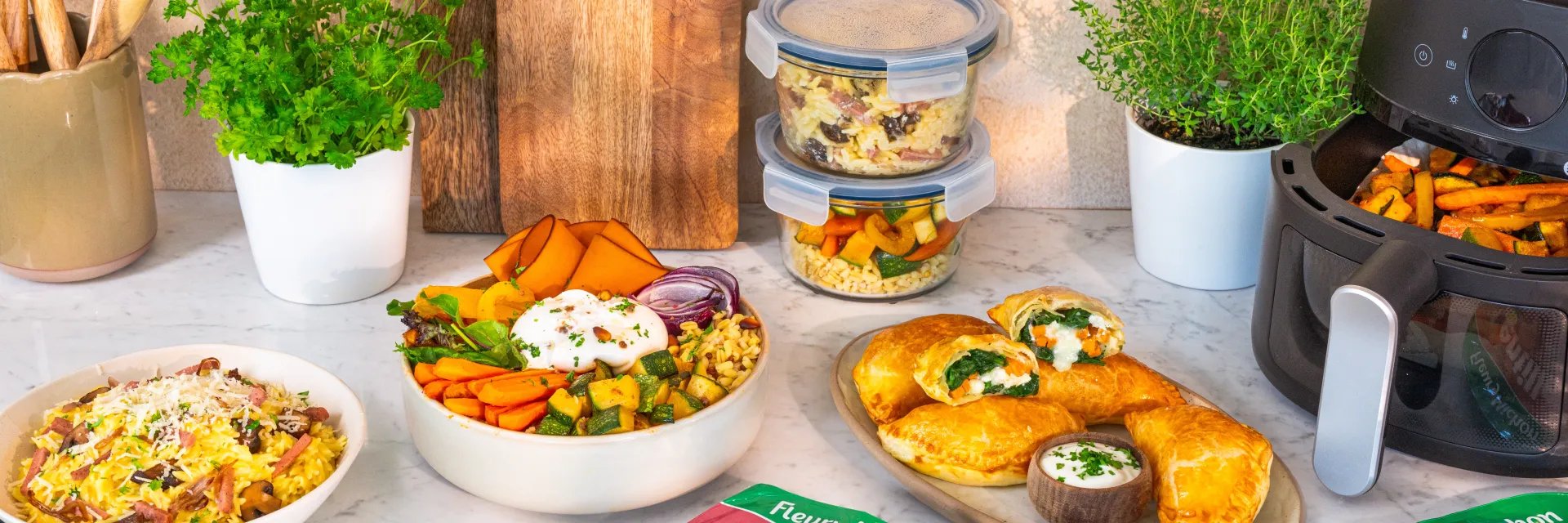 Repas prêt sur plan de travail: bols de légumes colorés, chaussons dorés, friteuse noire, packaging Fleury Michon