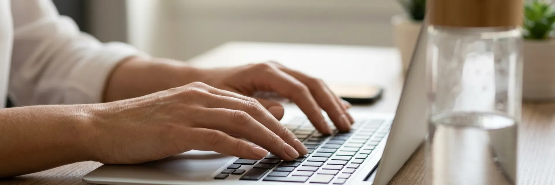 Mains de femme au vernis élégant tapant sur un clavier au bureau avec un verre d'eau