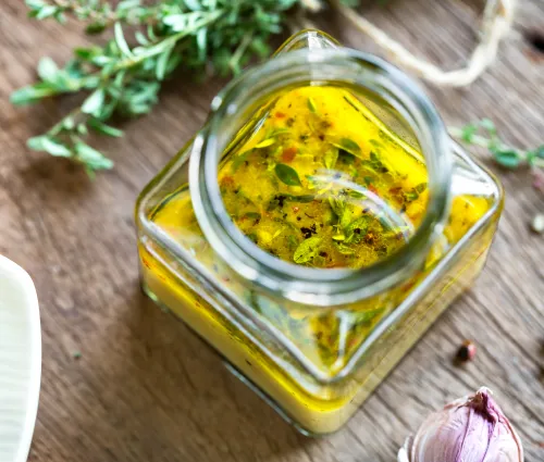 vinaigrette dans un pot en verre avec des herbes aromatiques posée sur un plan de travail en bois, entourée d'aromates 