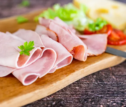 tranches de jambon posées sur sur une planche avec des crudités 