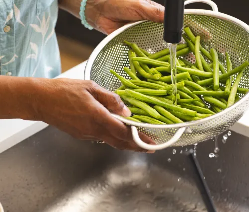 une femme tenant une passoire avec des haricots verts frais pour une fiche astuce Fleury Michon sur comment bien préparer les haricots verts