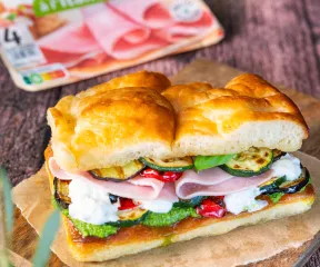 sandwich focaccia, jambon, burrata crémeuse, courgettes grillées, poivrons rouges confits, roquette, pesto, pain doré, texture croustillante, cœur fondant, cuisine méditerranéenne, planche en bois, lumière naturelle, ambiance chaleureuse, food gourmand