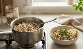 Casserole inox fumante de quinoa tricolore en cuisson sur plaque, cuillère, bol garni de citron et herbes sur plan de travail